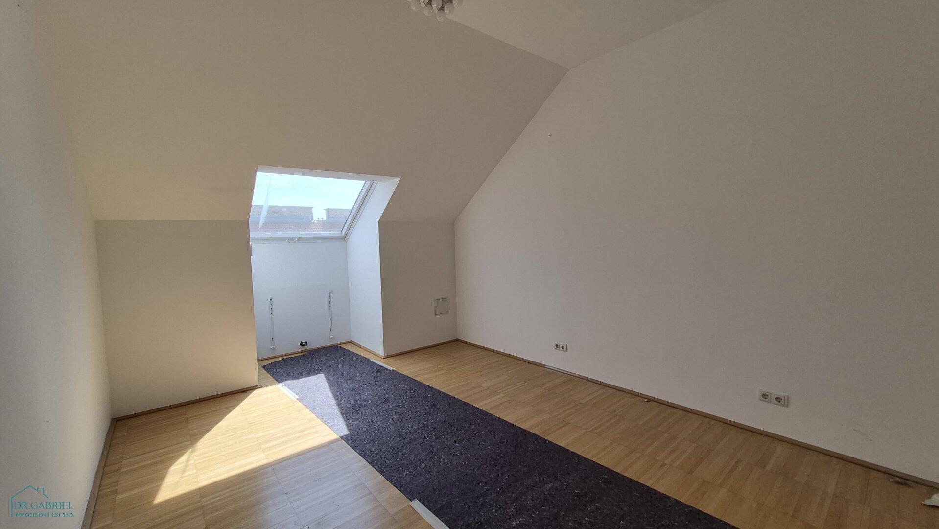 Heller Raum mit Parkettboden, Dachschrägen und einem großen Dachfenster für viel Tageslicht.