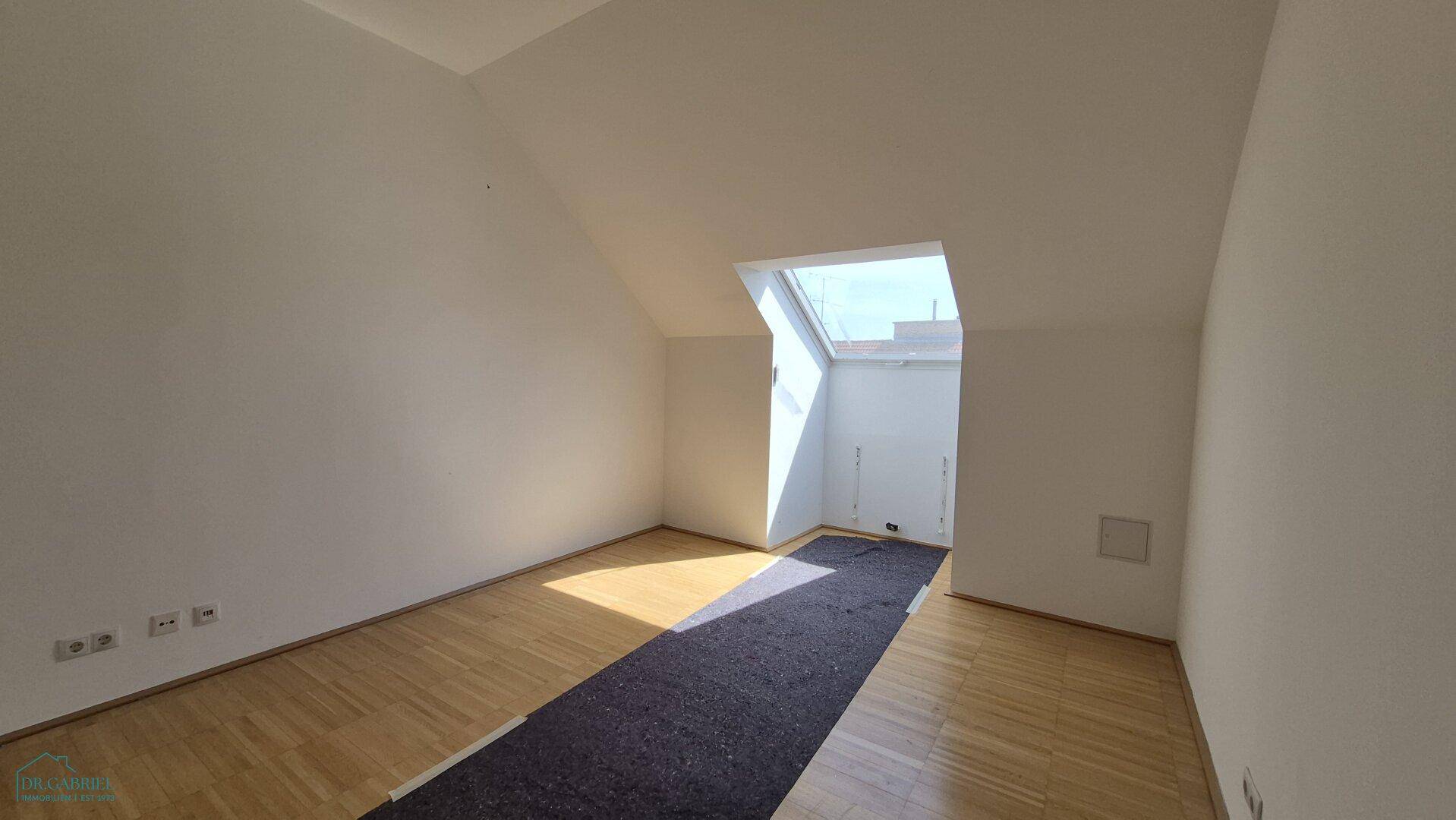 Lichtdurchfluteter Raum mit Parkettboden, Dachschrägen und einem großen Dachfenster.