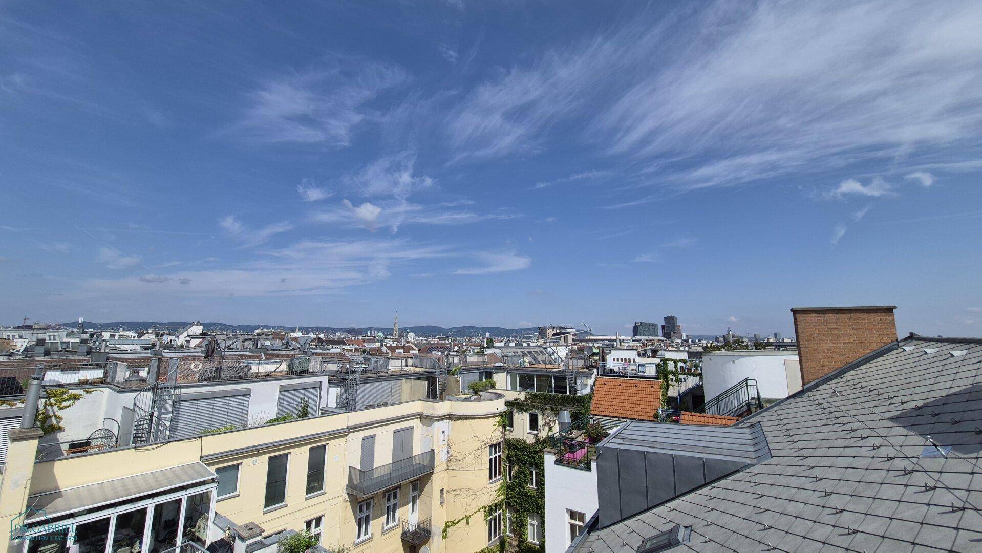 Weitläufiger Blick über die Dächer der Stadt unter einem klaren blauen Himmel.