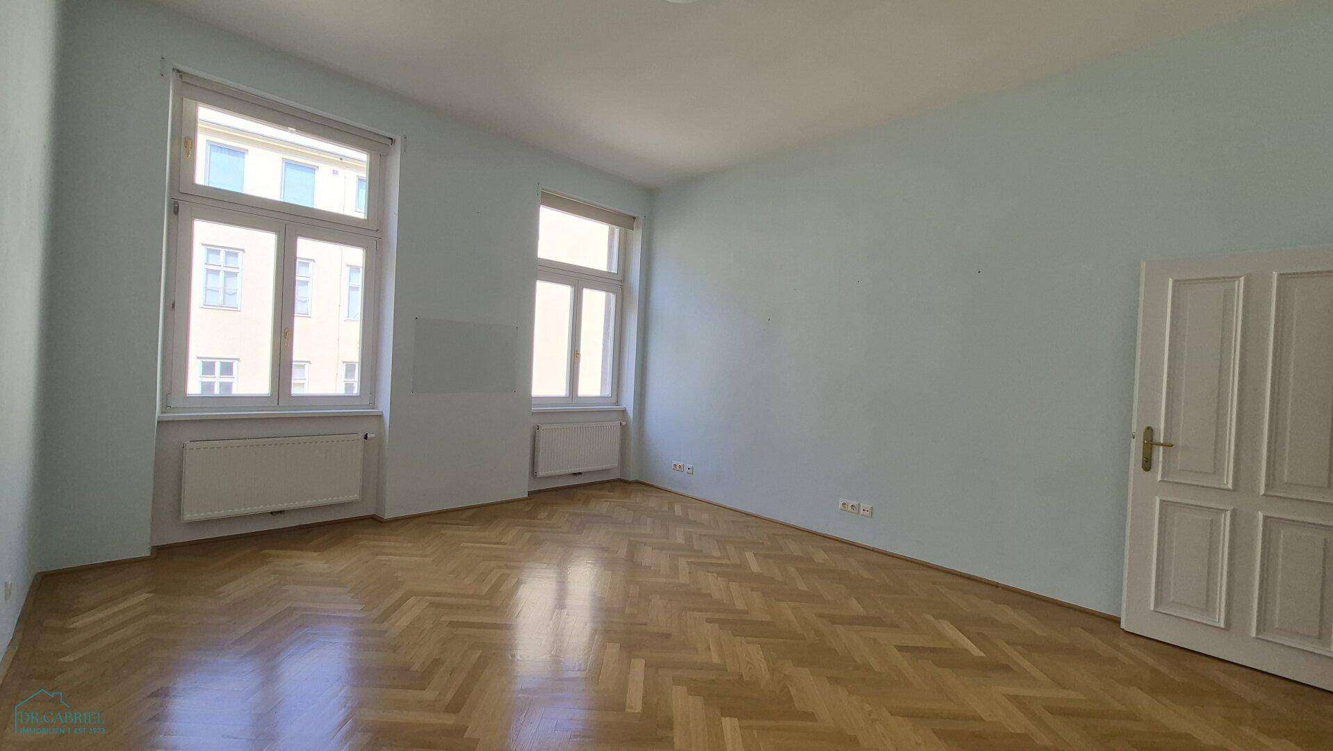 Geräumiges Zimmer mit hellblauen Wänden und Fischgrätparkett, vielseitig nutzbar.