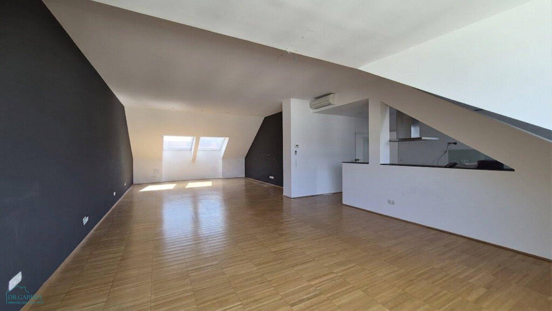 Heller, leerer Wohn-Essbereich mit Parkettboden, Dachschrägen und vorbereiteter Küchenzeile.