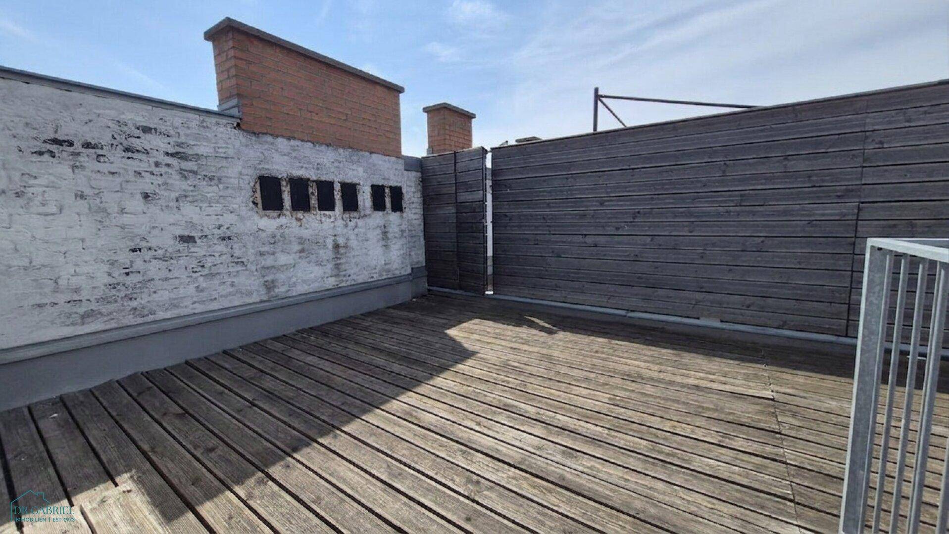 Leere Dachterrasse mit Holzbelag und einer Holzwand, bereit zur individuellen Gestaltung.