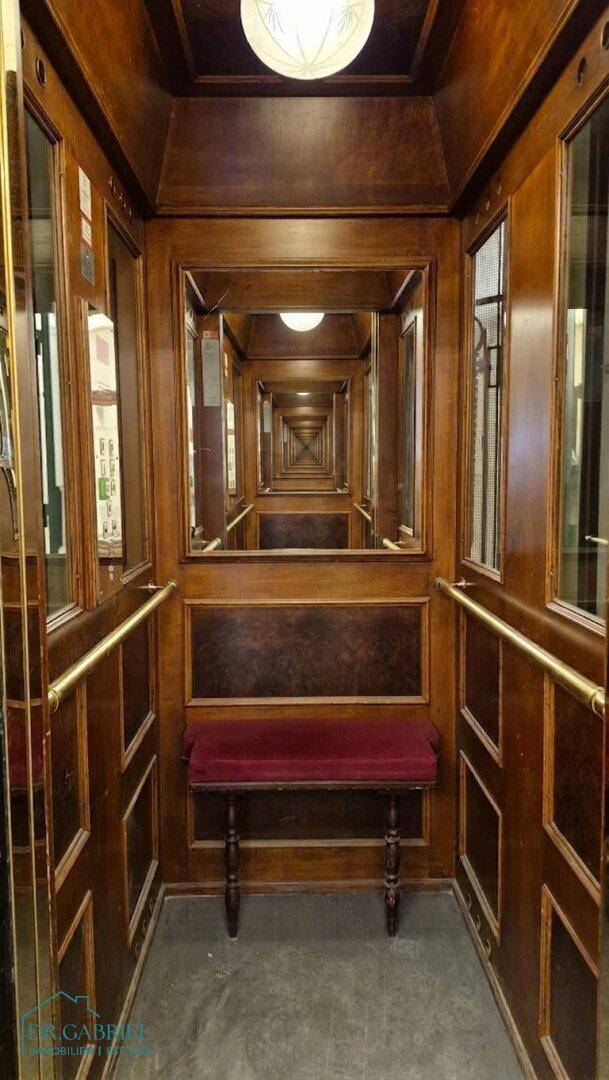 Elegante Aufzugskabine mit Holzvertäfelung, Spiegeln und einer Sitzbank, die einen luxuriösen Eindruck vermittelt.