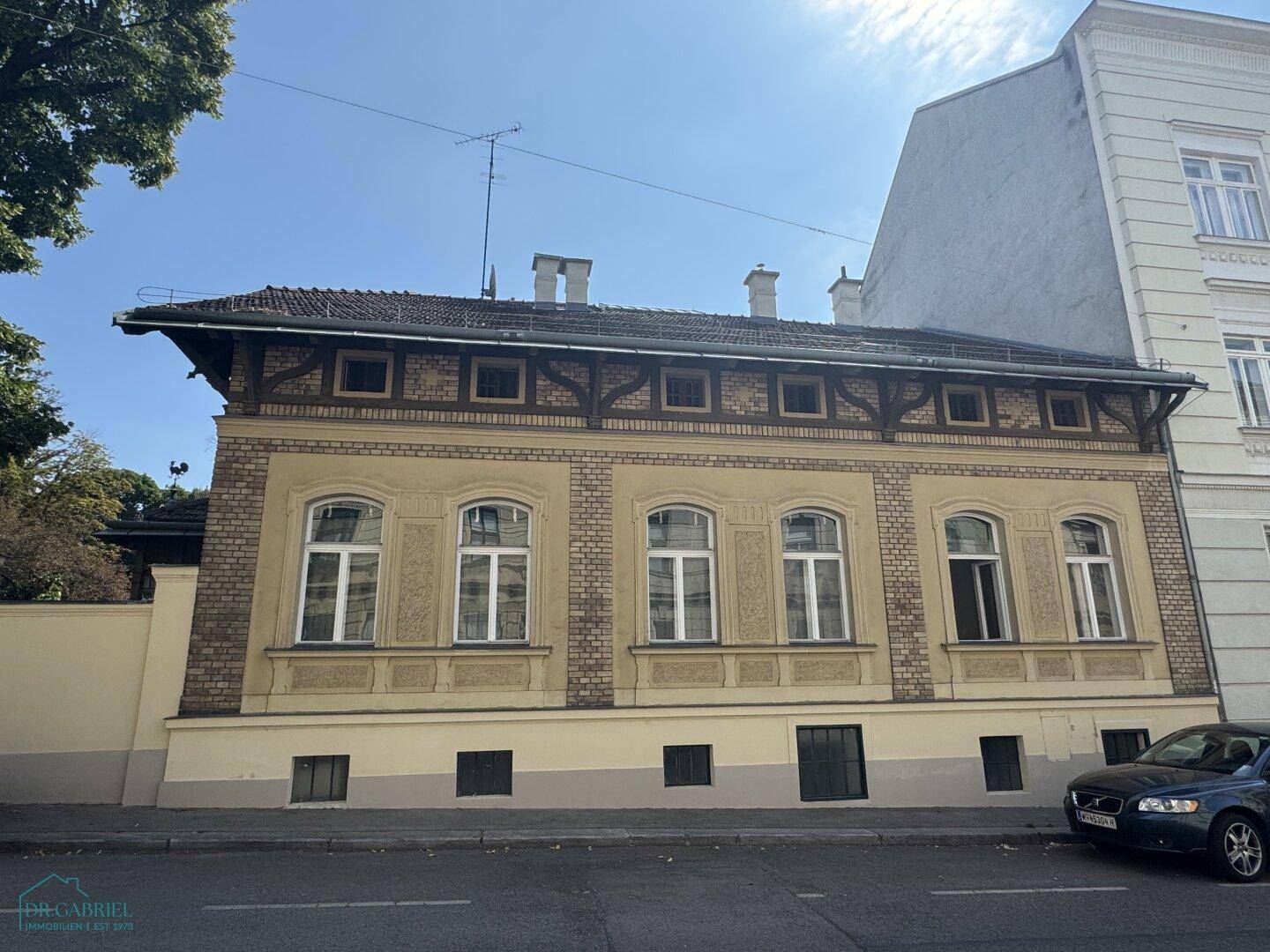Historisches Gebäude mit traditioneller Fassade, Holzbalken und mehreren Fenstern an einem sonnigen Tag.