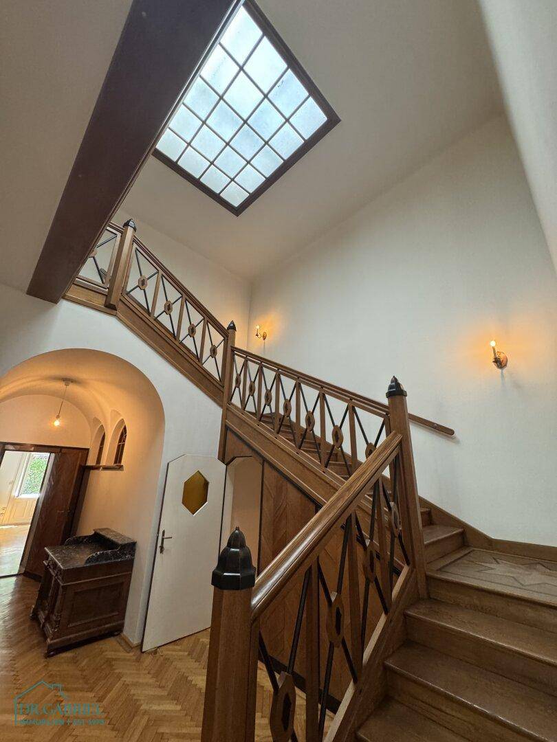 Elegantes Treppenhaus mit Holzgeländer, Fischgrätparkett und Oberlicht für natürliches Licht.