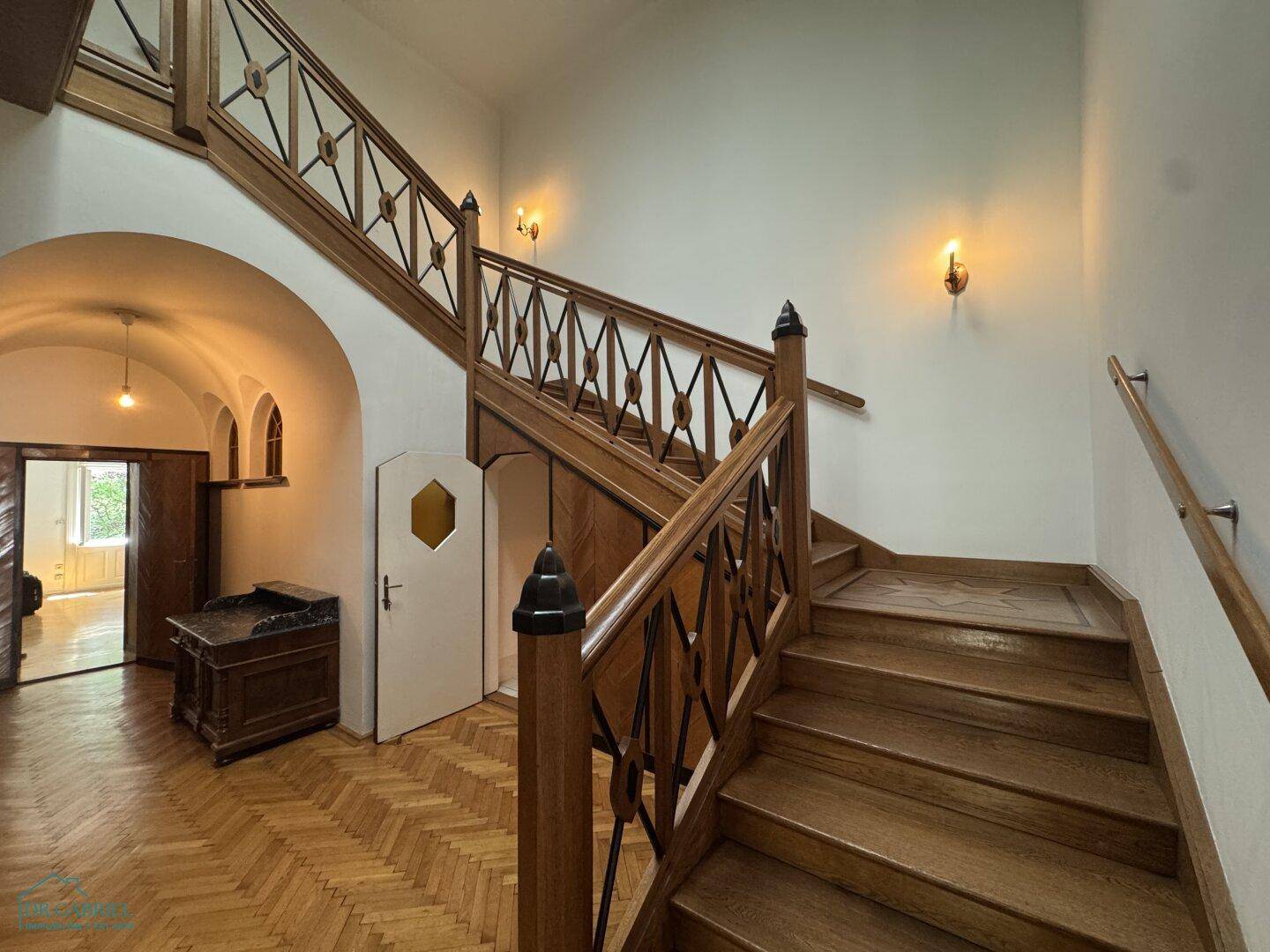 Klassisches Holztreppenhaus mit kunstvollem Geländer und Fischgrätparkett in einem historischen Gebäude.