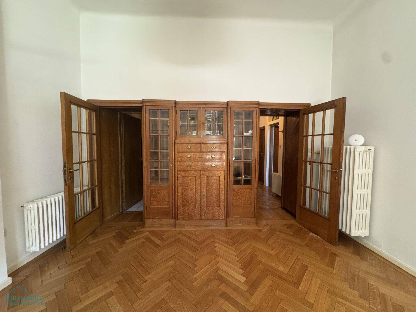 Geräumiges Zimmer mit Fischgrätparkett und einer beeindruckenden Holztrennwand mit Glastüren.