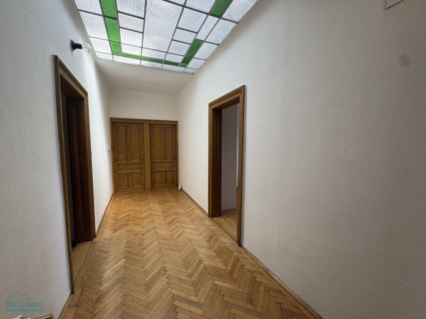 Heller Flur mit Fischgrätparkett und einem farbigen Oberlicht, das natürliches Licht spendet.