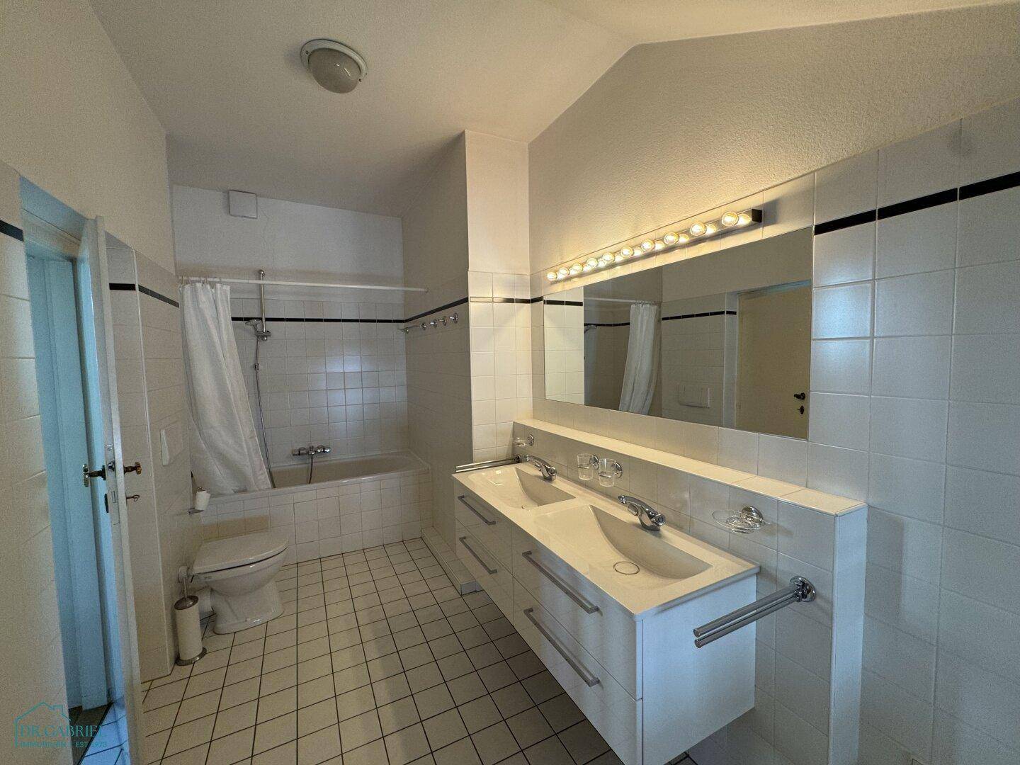 Modernes Badezimmer mit Doppelwaschbecken, Badewanne mit Duschvorhang und weißen Fliesen.