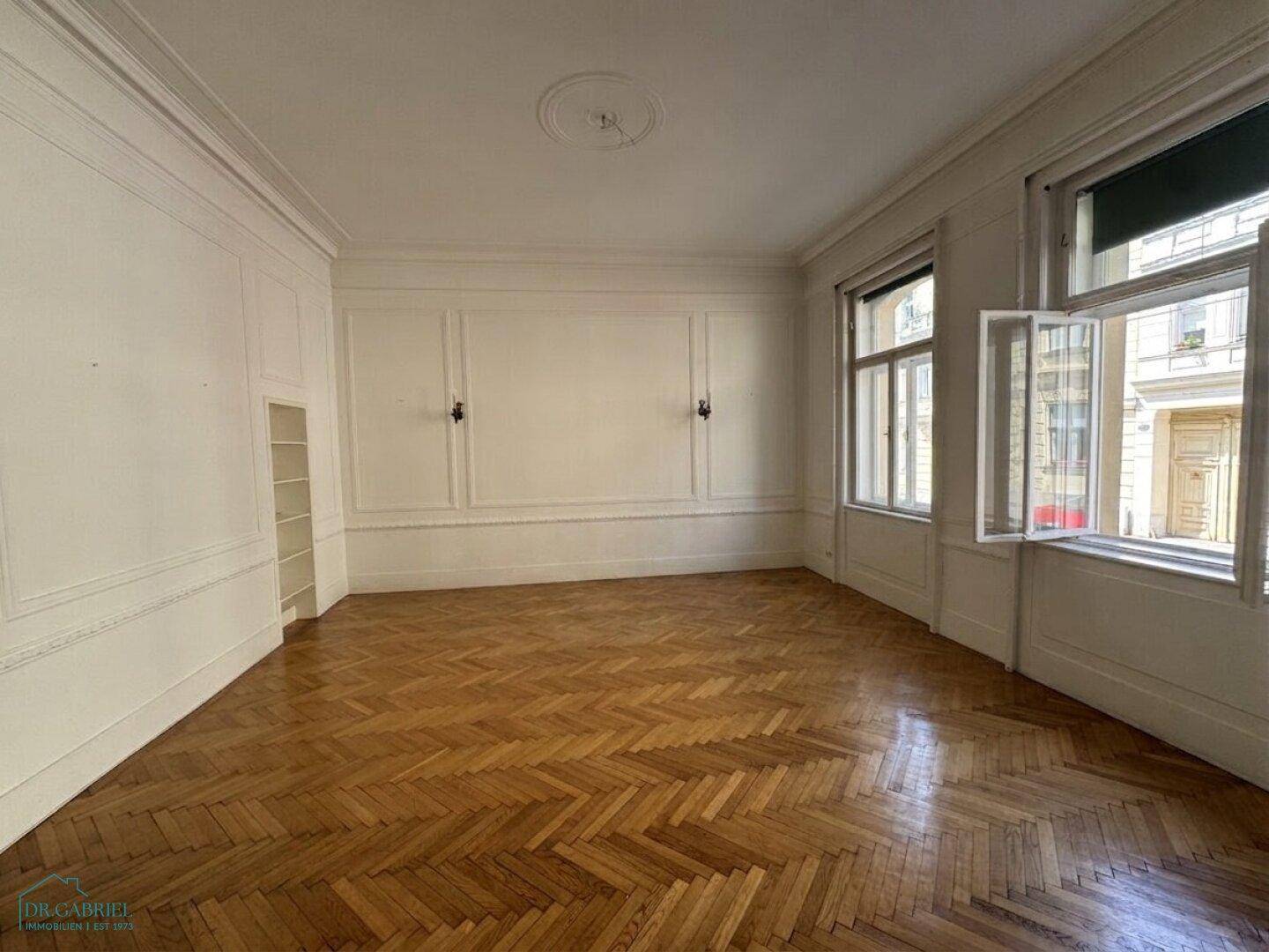 Helles Wohnzimmer mit klassischer Wandvertäfelung, Fischgrätparkett und Blick auf die Straße.