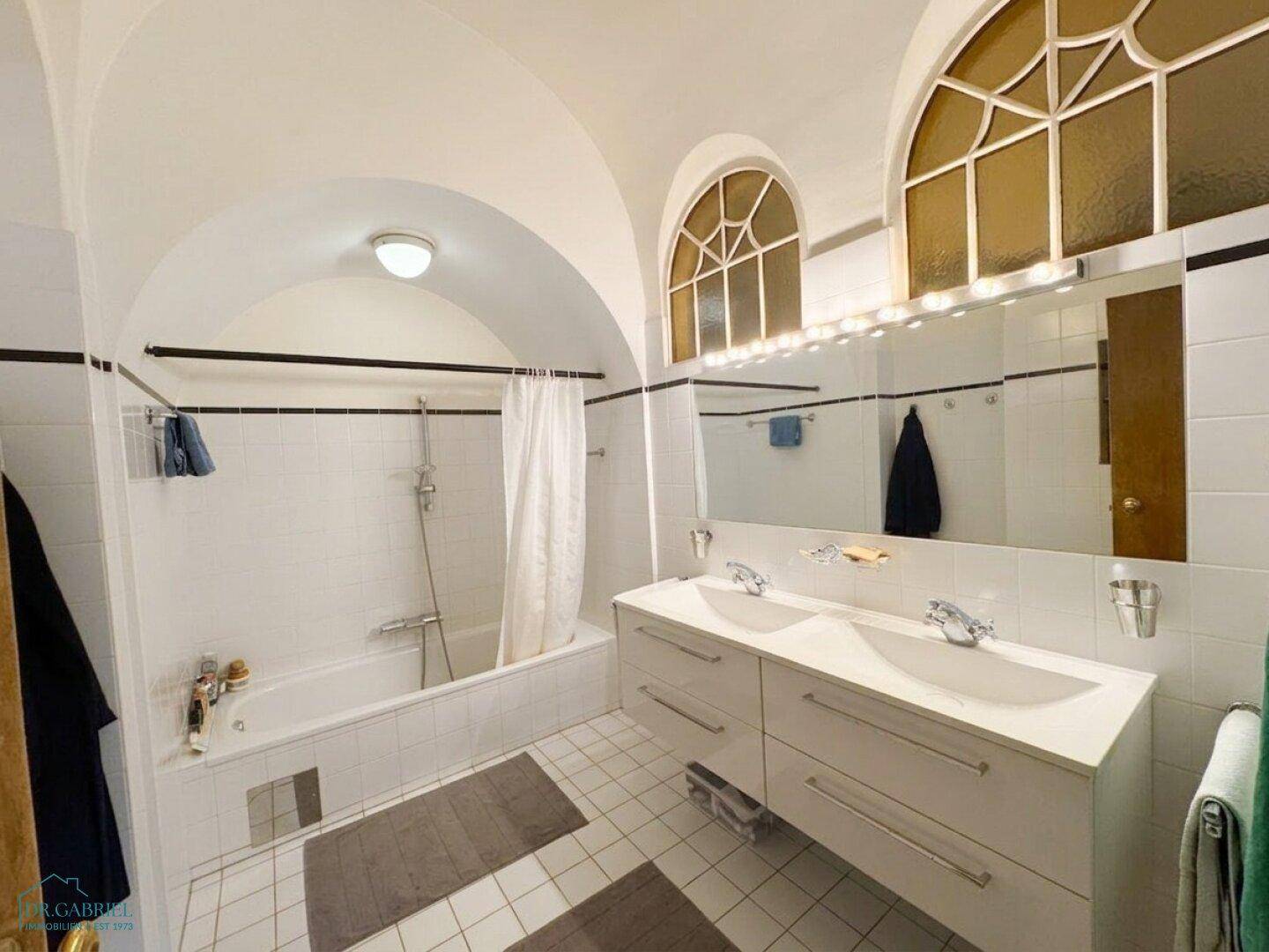 Modernes Badezimmer mit Doppelwaschbecken, Badewanne und gewölbter Decke.