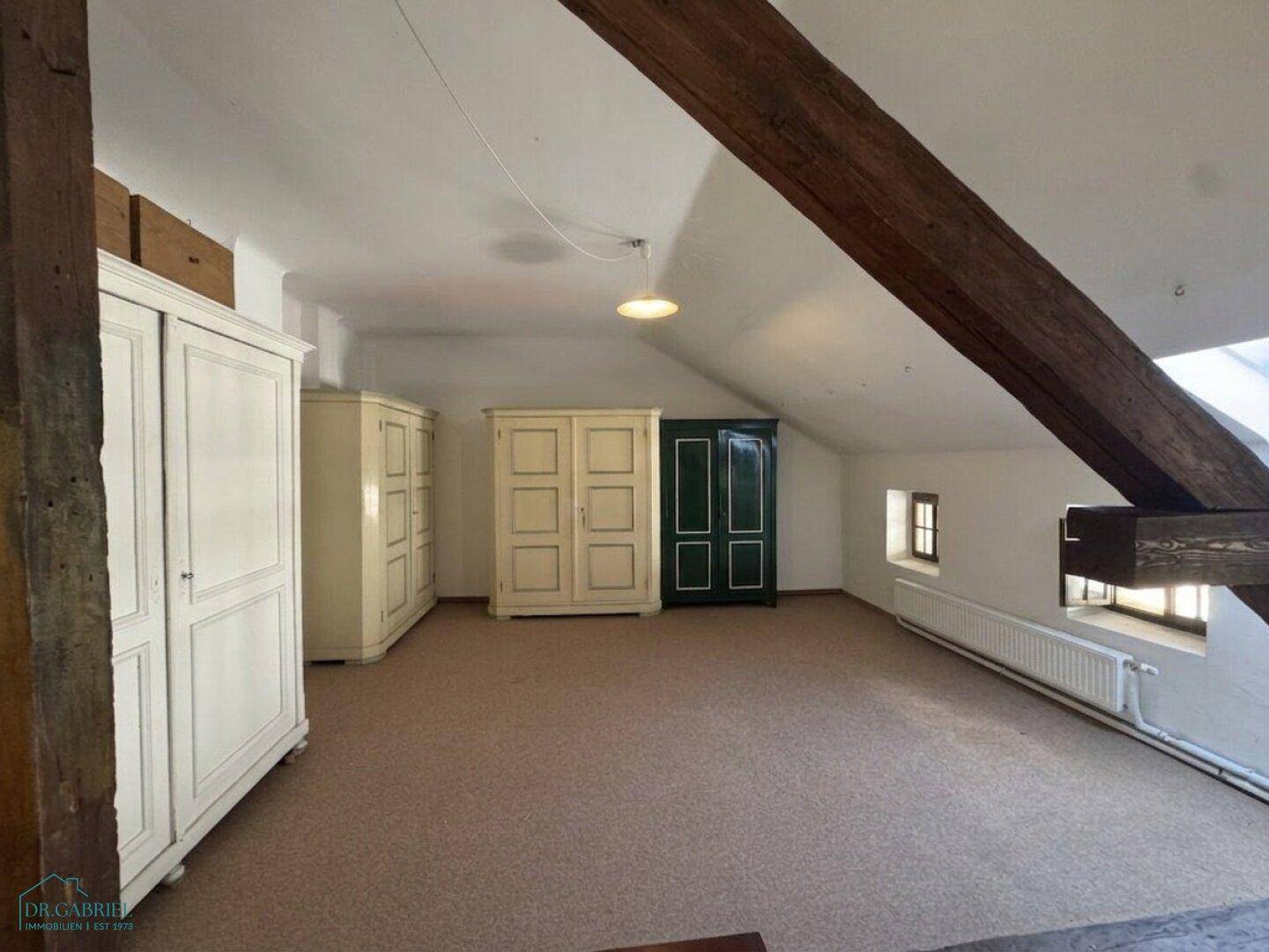 Ausgebauter Dachboden mit Teppichboden, sichtbaren Holzbalken und mehreren Schränken.
