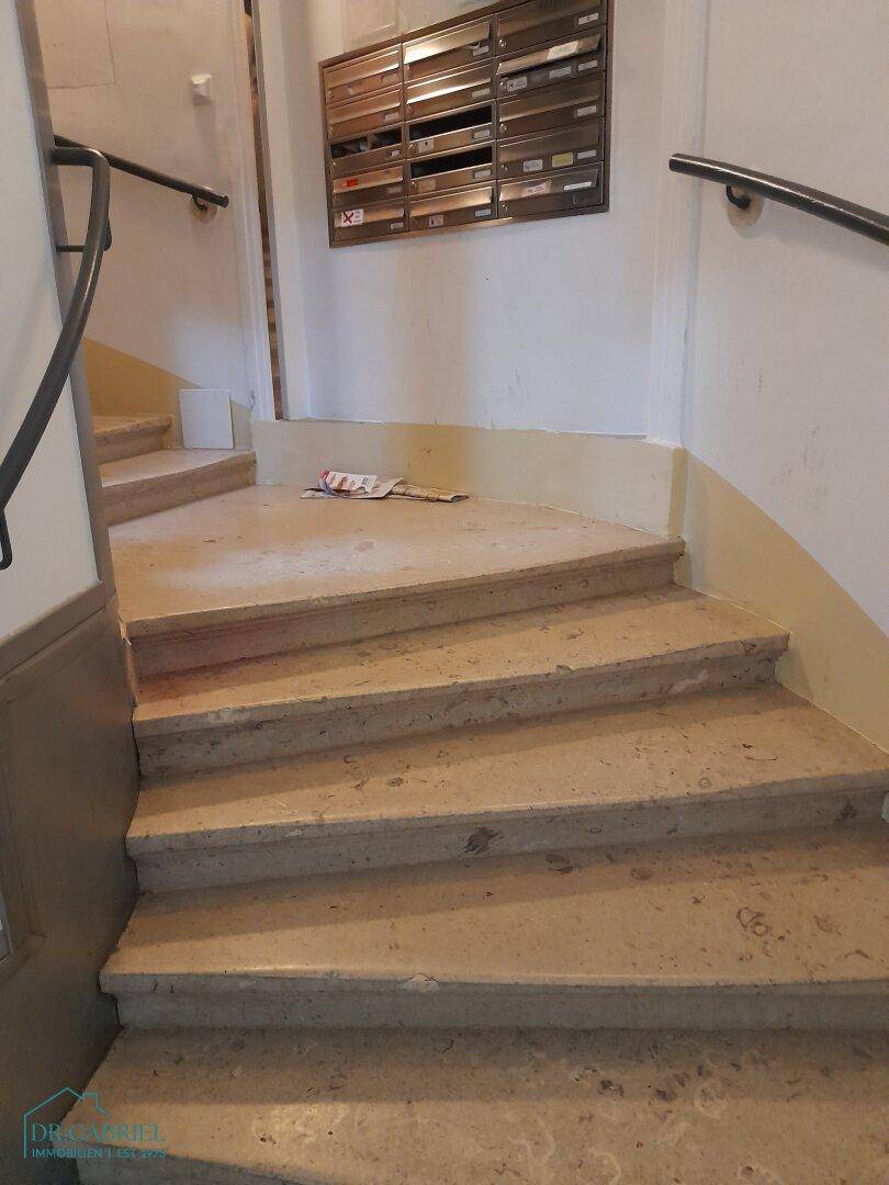 Treppenhaus eines Altbaus mit Steinstufen und Briefkästen im Eingangsbereich.
