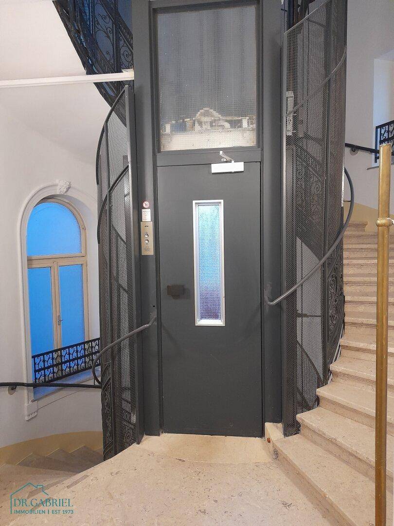 Historisches Treppenhaus mit modernem Aufzug und eleganten Steinböden.