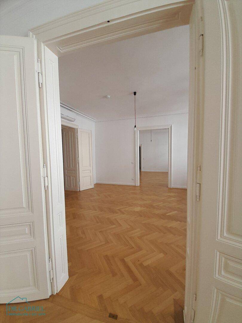 Blick durch eine offene Flügeltür in einen weiteren Raum mit elegantem Fischgrätparkett.