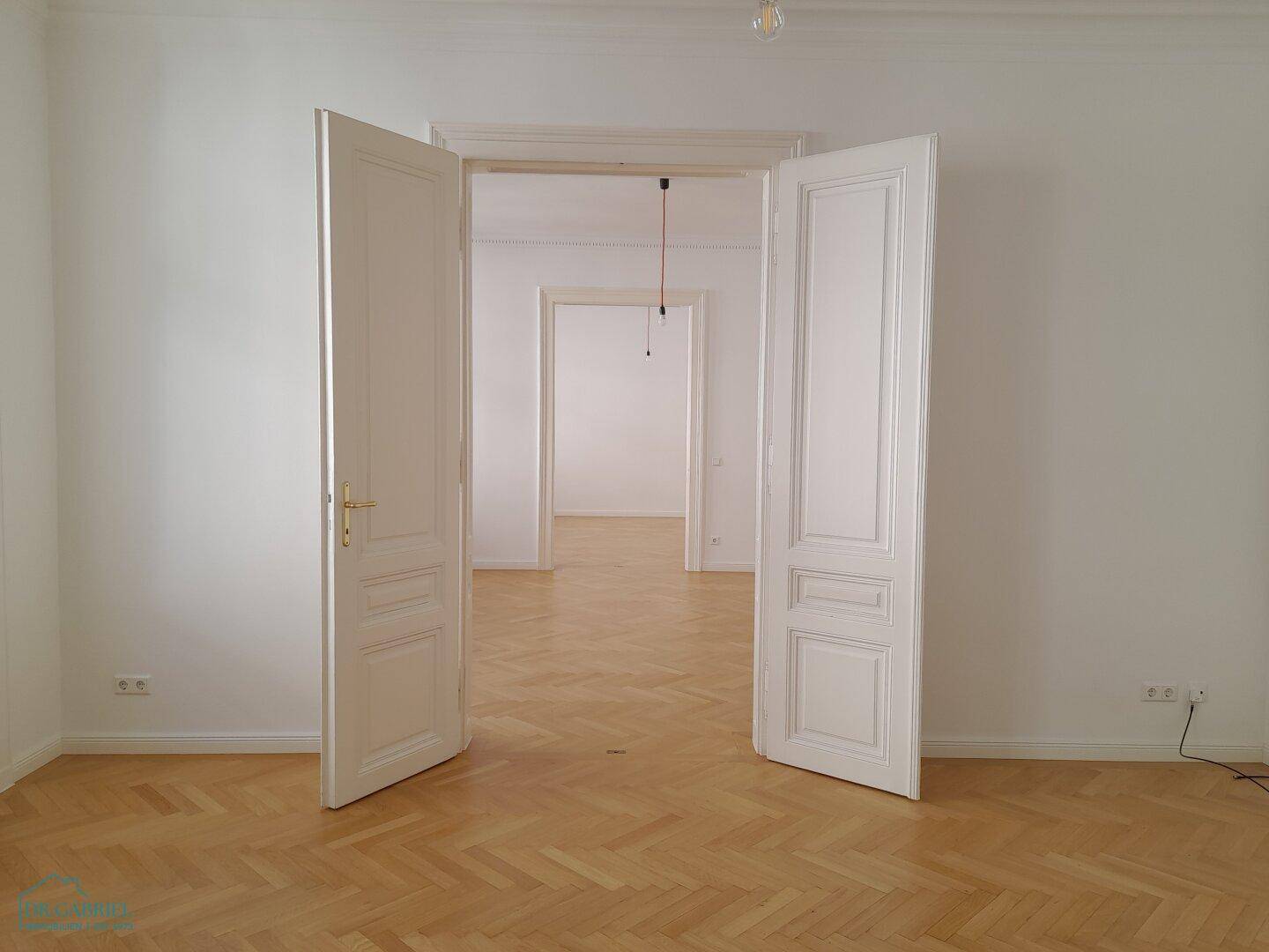 Geräumiger Flur mit klassischem Fischgrätparkett und hohen Flügeltüren, der mehrere Zimmer verbindet.