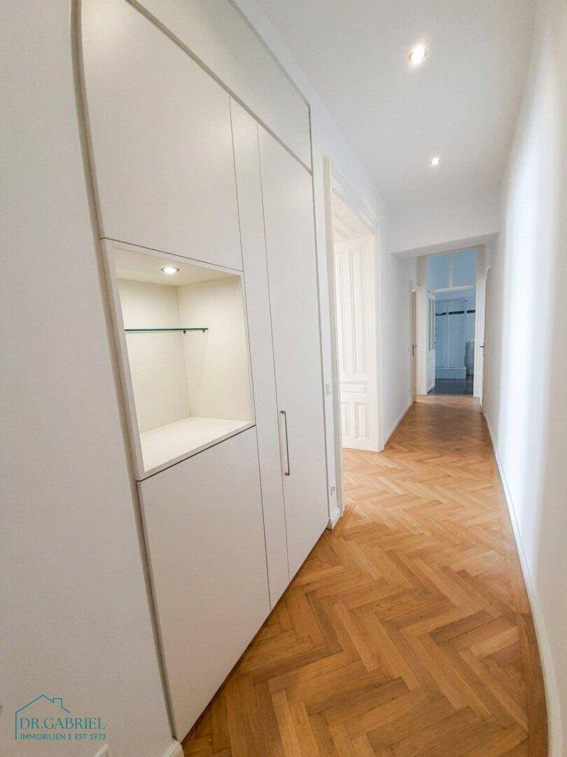 Langer Flur mit Einbauschränken und Fischgrätparkett, der zu weiteren Räumen führt.