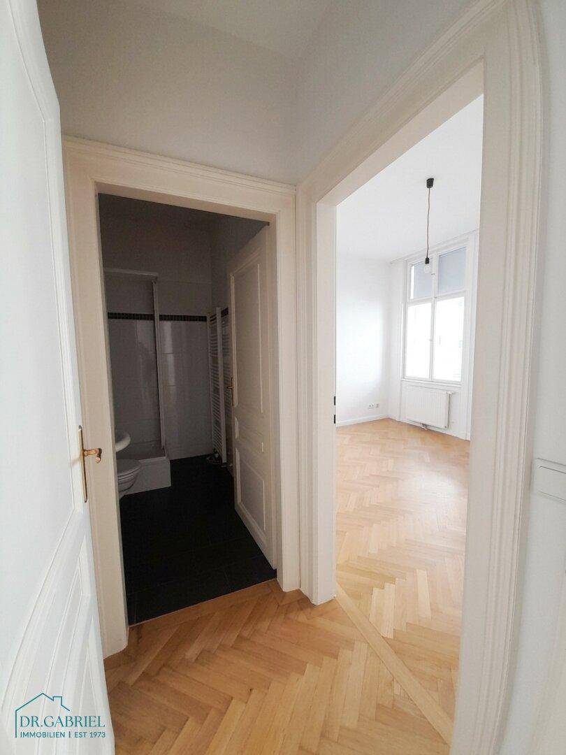 Flur mit Fischgrätparkett, der zu einem Badezimmer und einem weiteren Zimmer führt.