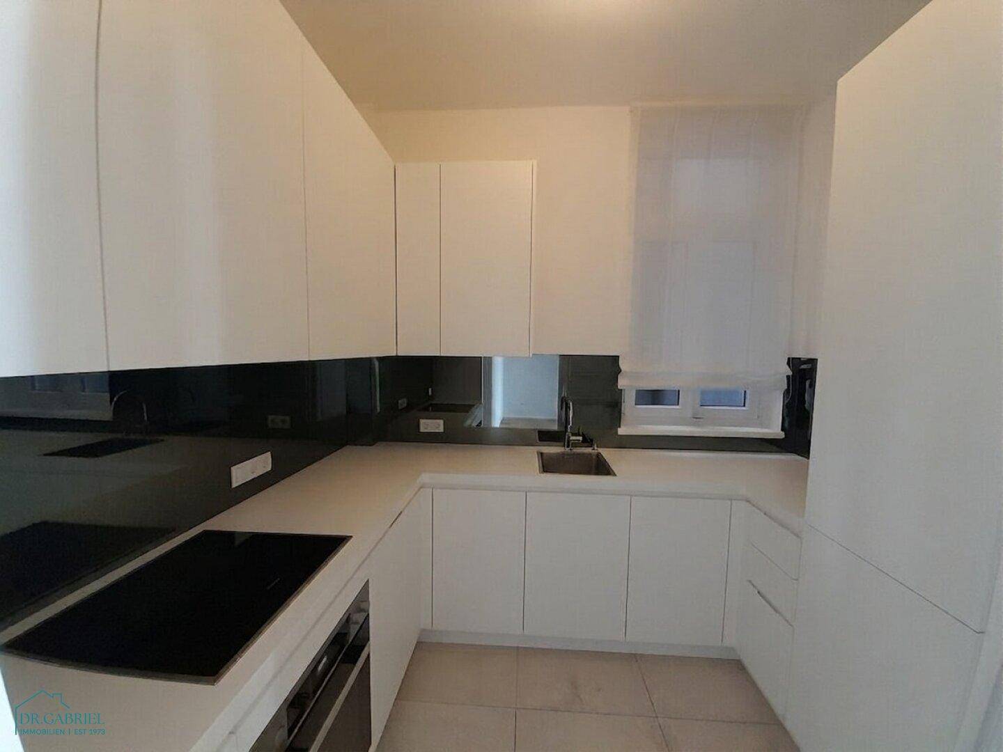 Moderne Einbauküche mit weißen Schränken, Induktionskochfeld und dunkler Rückwand.