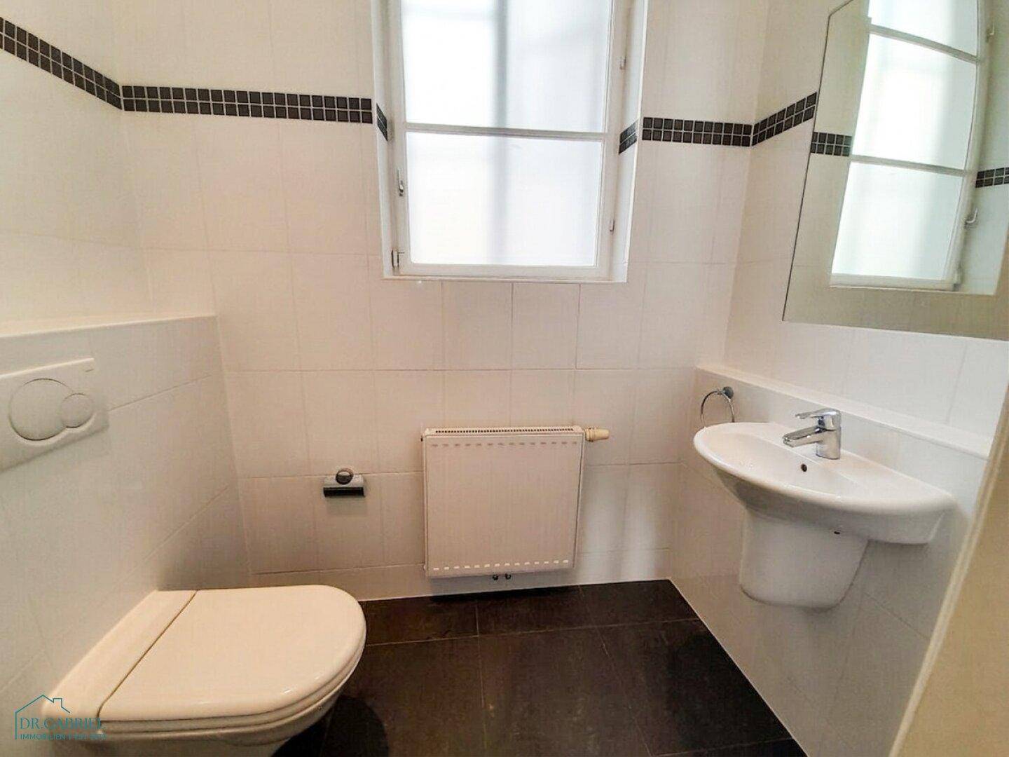Kleines Gäste-WC mit Fenster, Waschbecken und Wand-WC, ausgestattet mit dunklen Bodenfliesen.