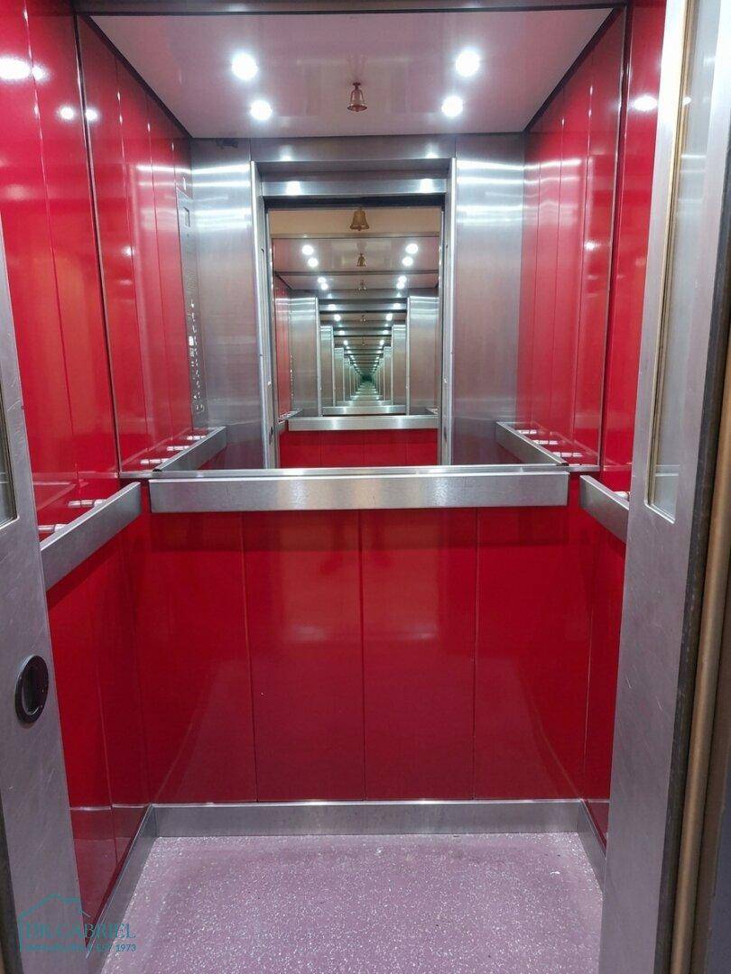 Innenansicht eines modernen Aufzugs mit roten Wänden und Spiegeln.