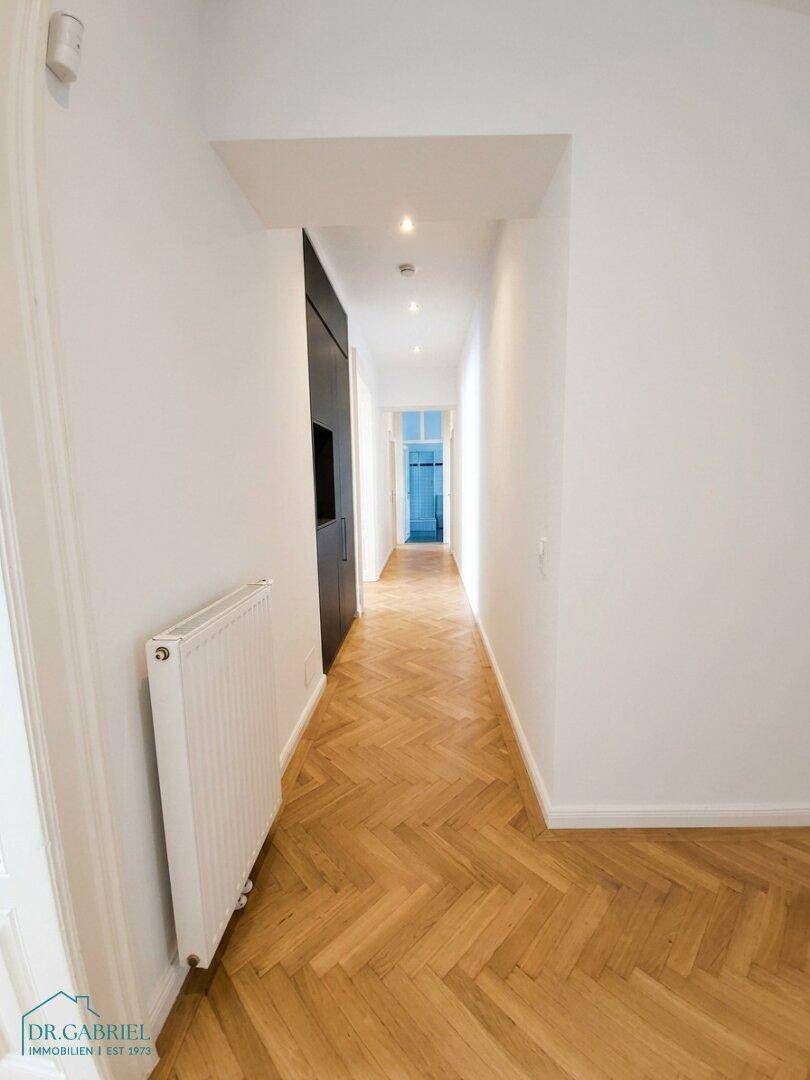 Schmaler Flur mit Fischgrätparkett und Deckenstrahlern, der in die Tiefe des Apartments führt.