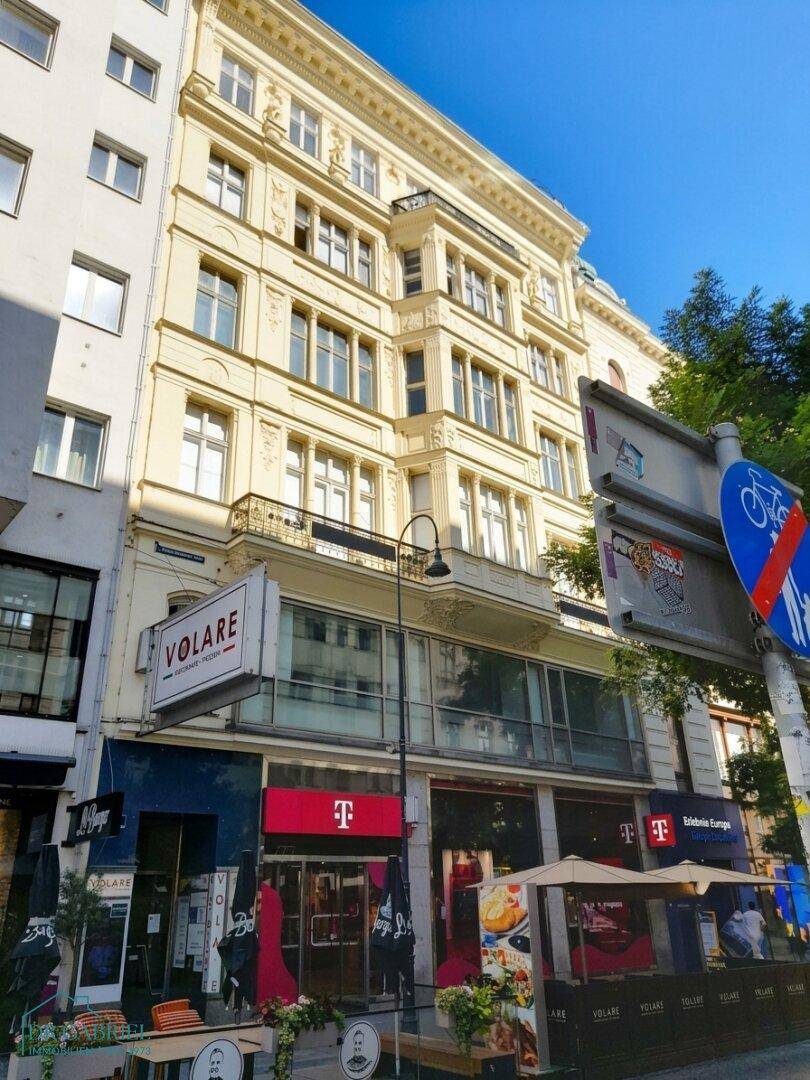 Historisches Gebäude mit eleganter Fassade und Geschäften im Erdgeschoss an einer belebten Straße.