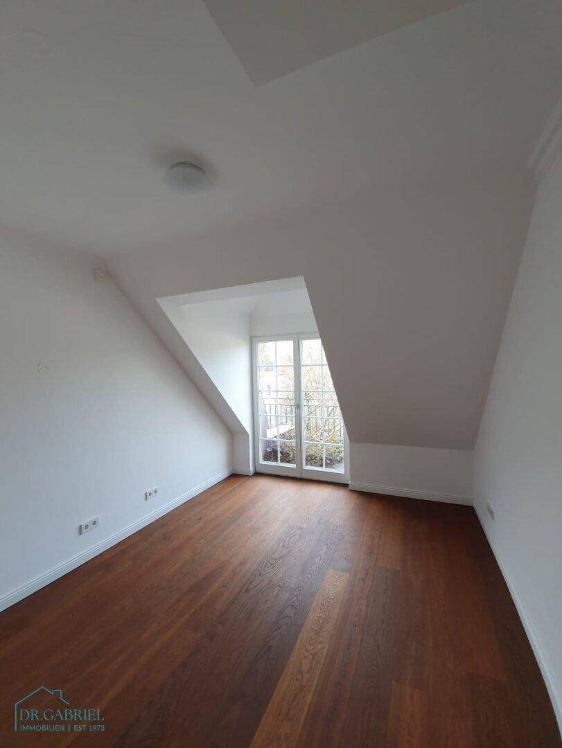 Geräumiges Schlafzimmer mit Holzboden, Dachschrägen und Zugang zu einem französischen Balkon.