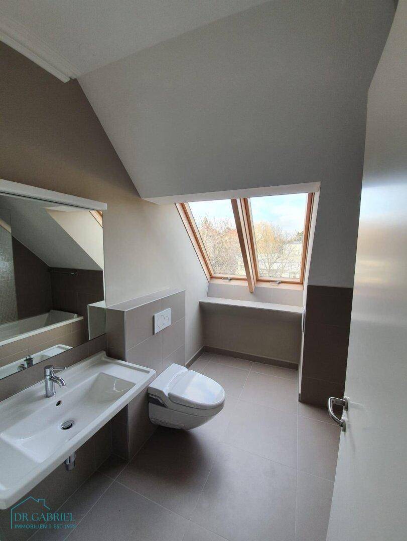 Helles Badezimmer mit Dachfenstern, modernem WC, Einzelwaschbecken und grauen Fliesen.