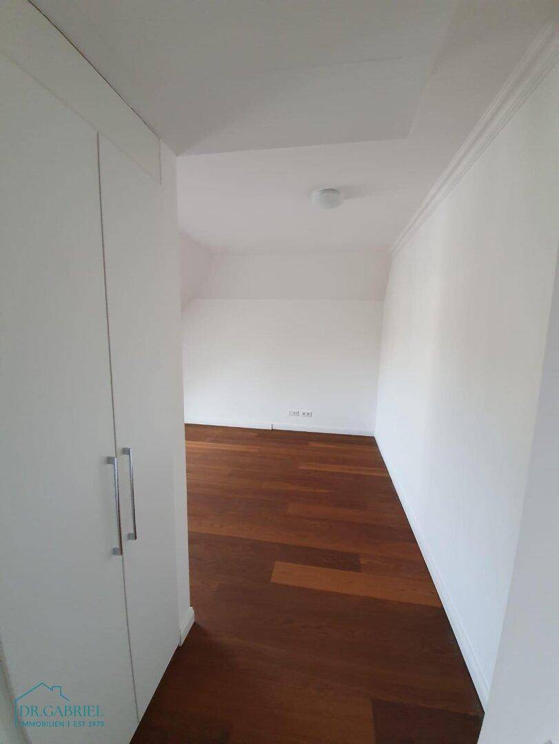 Heller Flur mit Einbauschränken und Holzboden, der zu einem weiteren Raum führt.