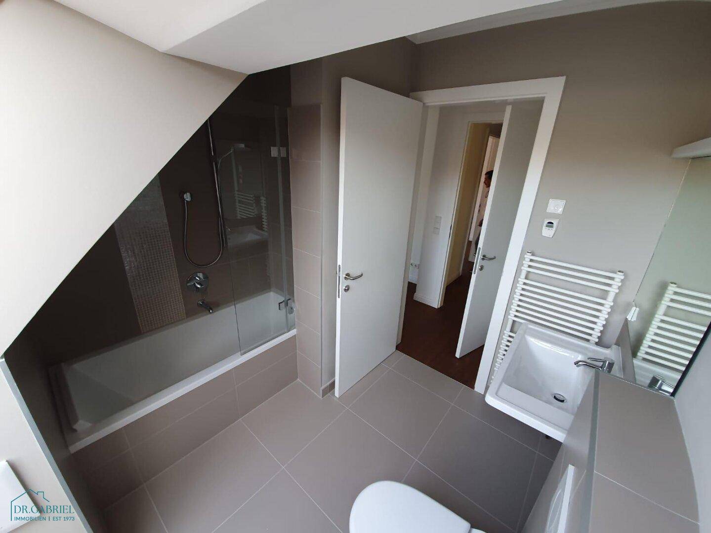 Modernes Badezimmer mit Badewanne, Dusche, Einzelwaschbecken und beheiztem Handtuchhalter.
