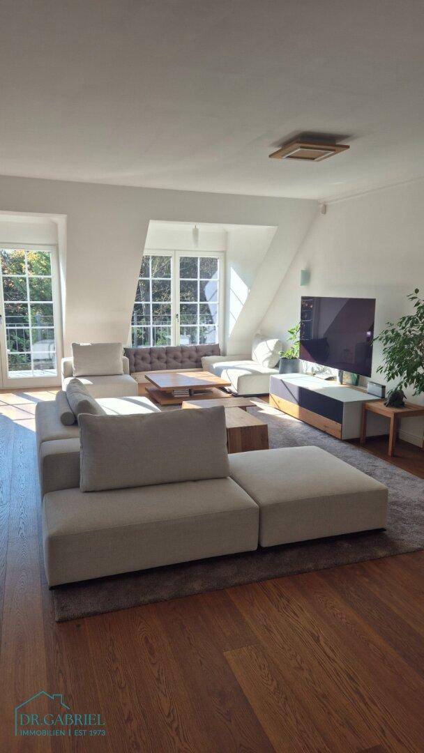 Helles Wohnzimmer mit Holzboden, bequemer Couch und Blick ins Grüne durch große Fenster.