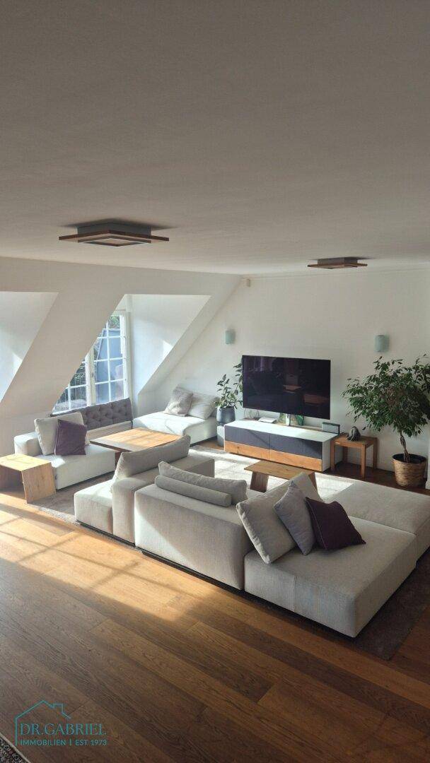 Geräumiges Wohnzimmer mit moderner Einrichtung, Holzboden und viel Tageslicht durch Dachschrägenfenster.