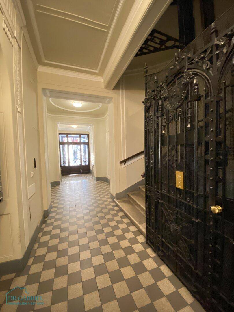Historischer Hausflur mit Schachbrettmuster-Fliesenboden und einem kunstvollen Gitteraufzug.
