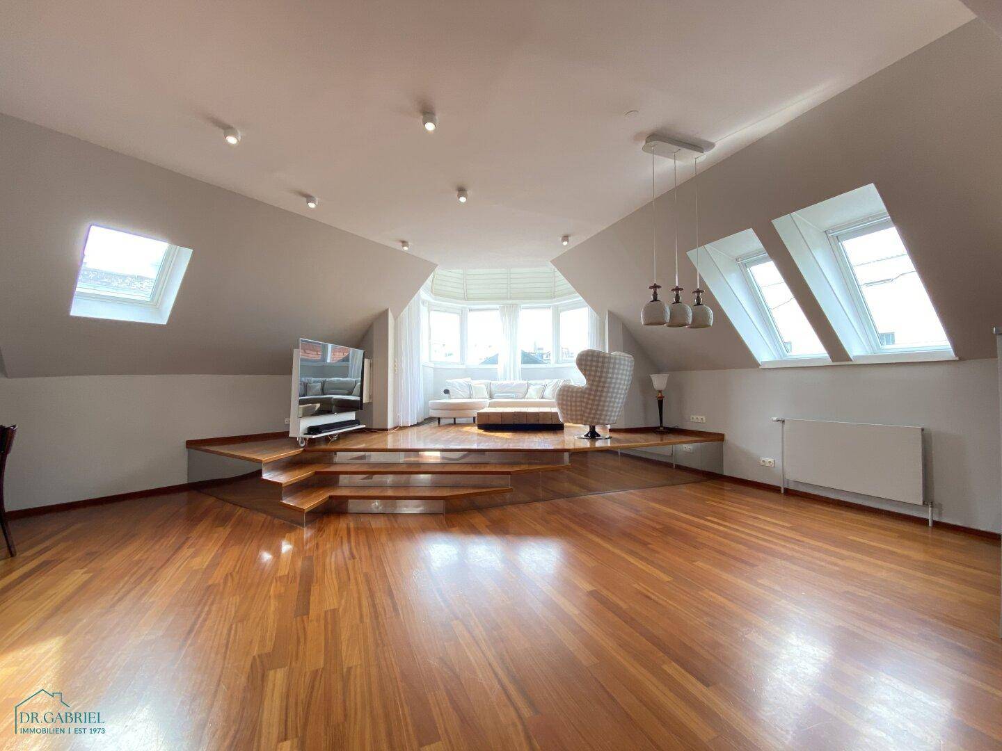 Geräumiges Wohnzimmer mit Holzboden, Dachschrägen und mehreren Dachfenstern für viel Licht.