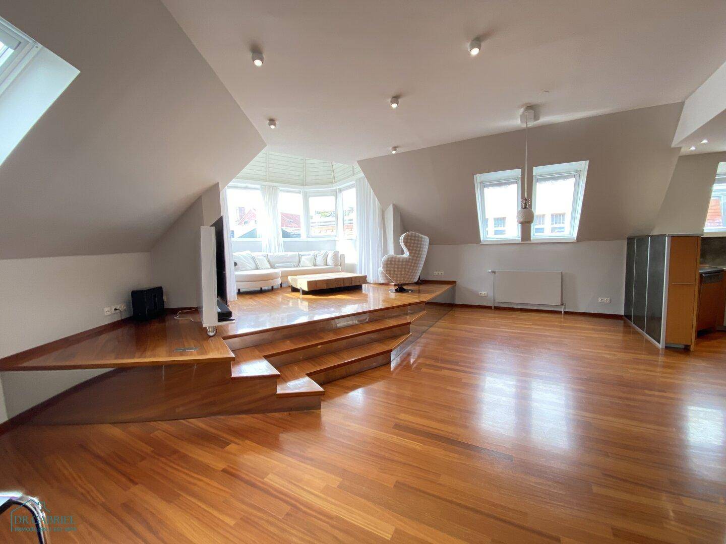 Heller Wohnbereich mit Holzboden, erhöhter Lounge-Zone und schrägen Wänden im Dachgeschoss.
