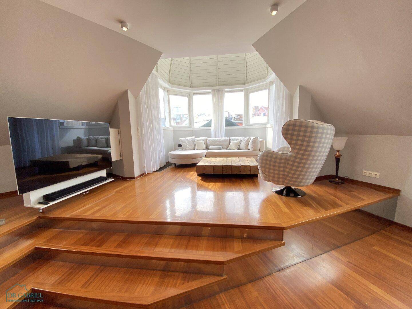 Großzügiges Wohnzimmer mit Holzboden, erhöhter Sitzecke und moderner Einrichtung.