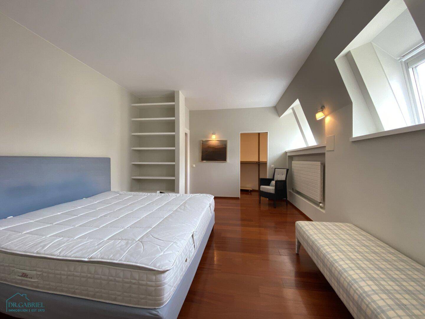 Geräumiges Schlafzimmer mit Holzboden, Einbauregalen und Dachfenstern.
