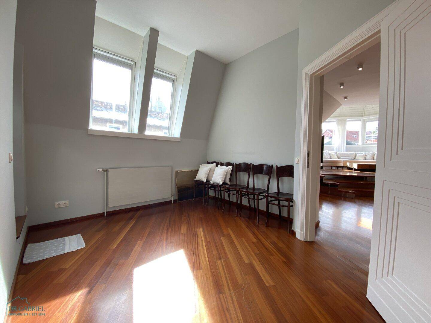 Helles Zimmer mit Holzboden, Dachschrägen und Blick auf die Stadt.