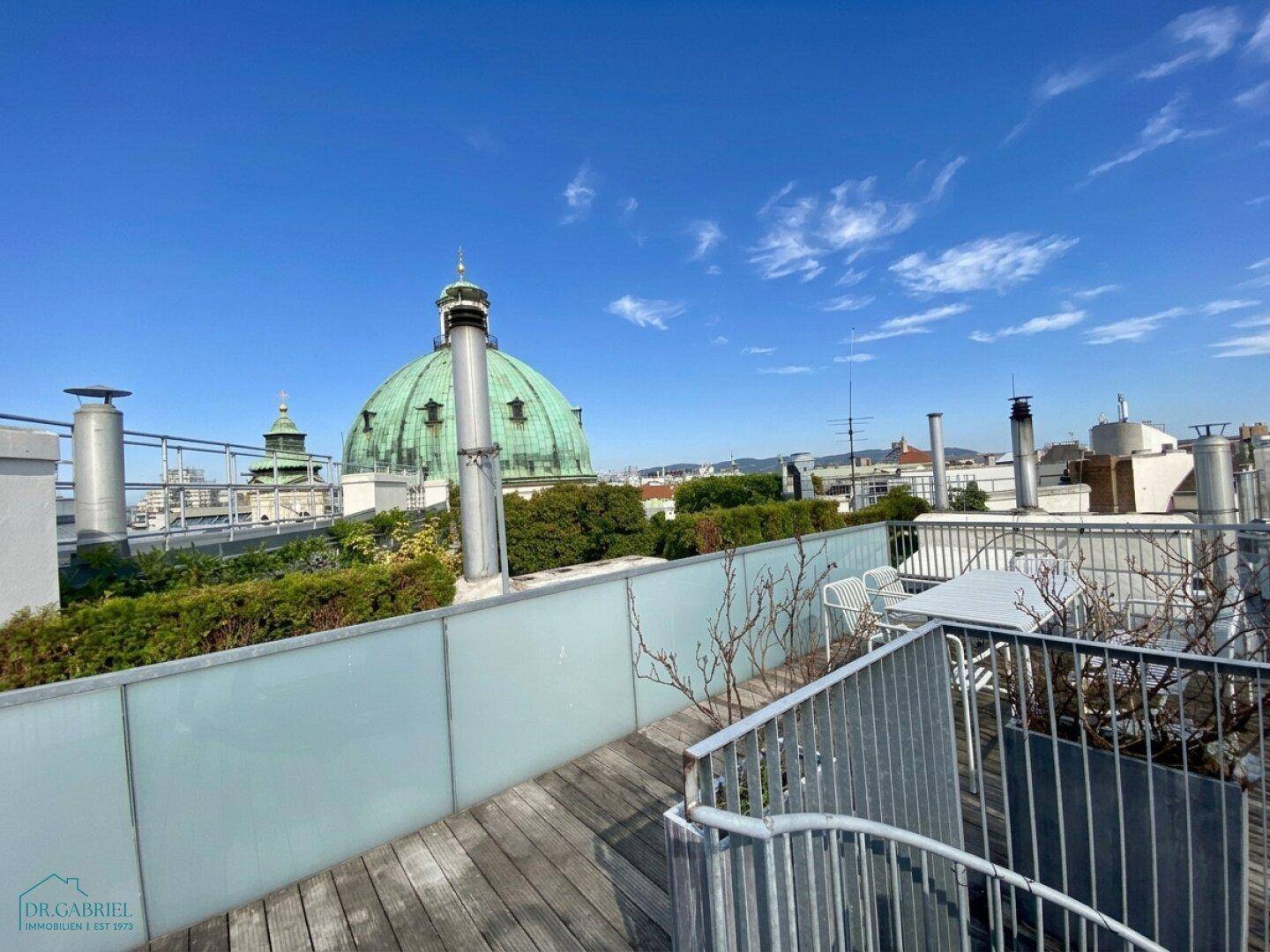 Geräumige Dachterrasse mit Holzboden und Panoramablick über die Dächer der Stadt.