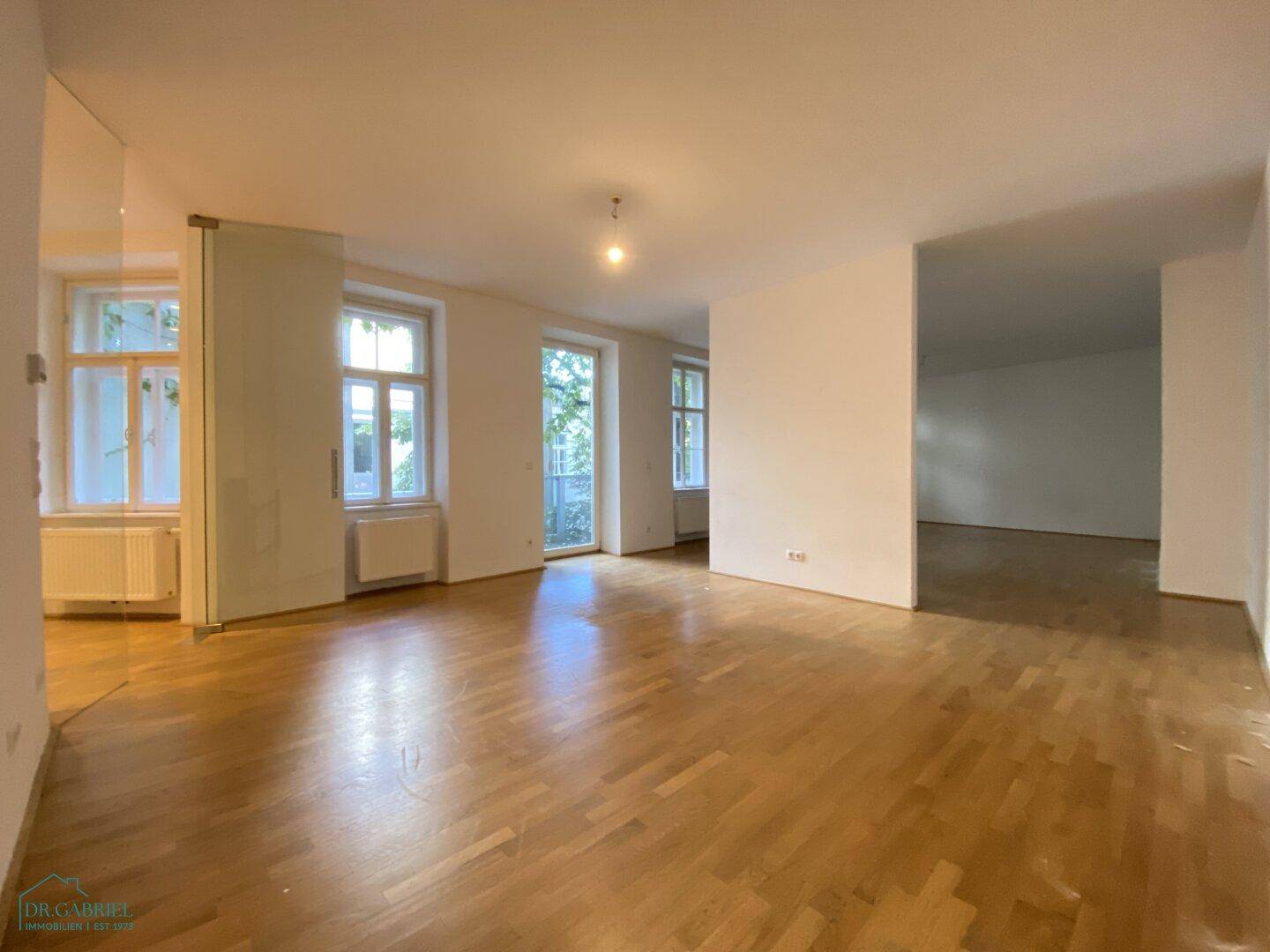 Großzügiger, heller Raum mit Holzboden und mehreren Fenstern, bereit für individuelle Gestaltung.