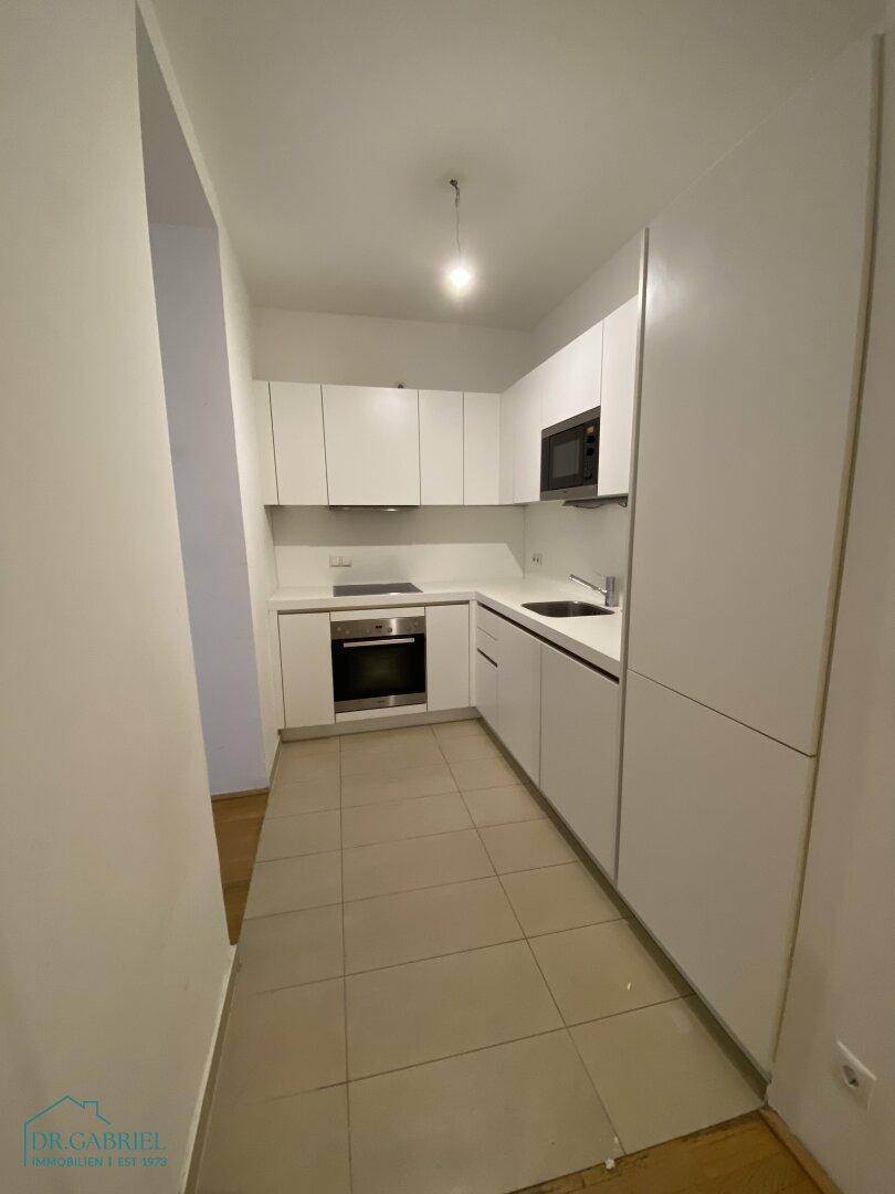 Moderne Einbauküche mit weißen Schränken, integrierten Geräten und Fliesenboden in hellem Farbton.