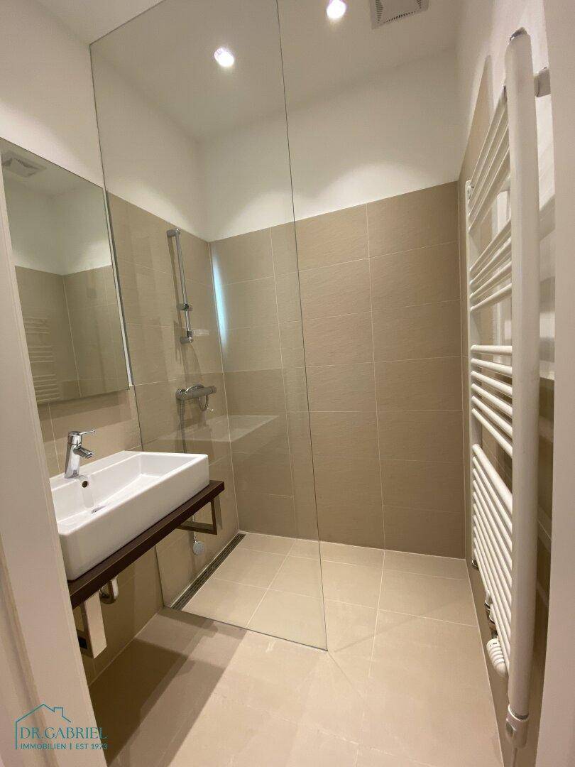 Modernes Badezimmer mit begehbarer Dusche, beigefarbenen Fliesen und beheiztem Handtuchhalter.