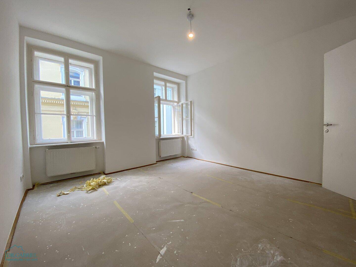 Leeres Schlafzimmer mit zwei großen Fenstern und vorbereitetem Unterboden für neue Bodenbeläge.