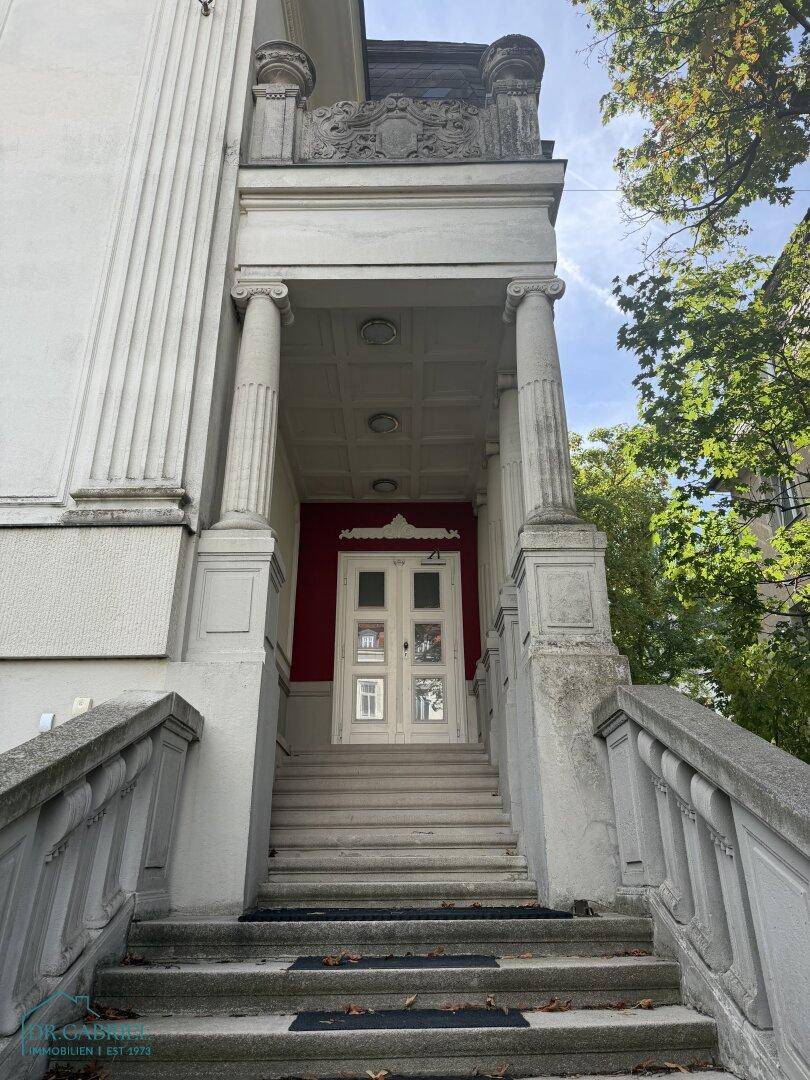 Prächtiger Eingangsbereich der Villa mit Steintreppe, Säulen und roter Akzentwand.