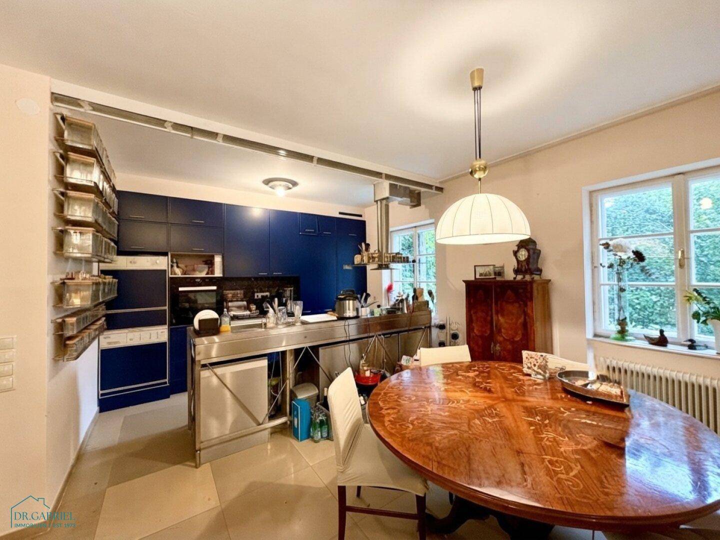Moderne Küche mit blauen Schränken, Edelstahlinsel und großem Holzesstisch im Essbereich.