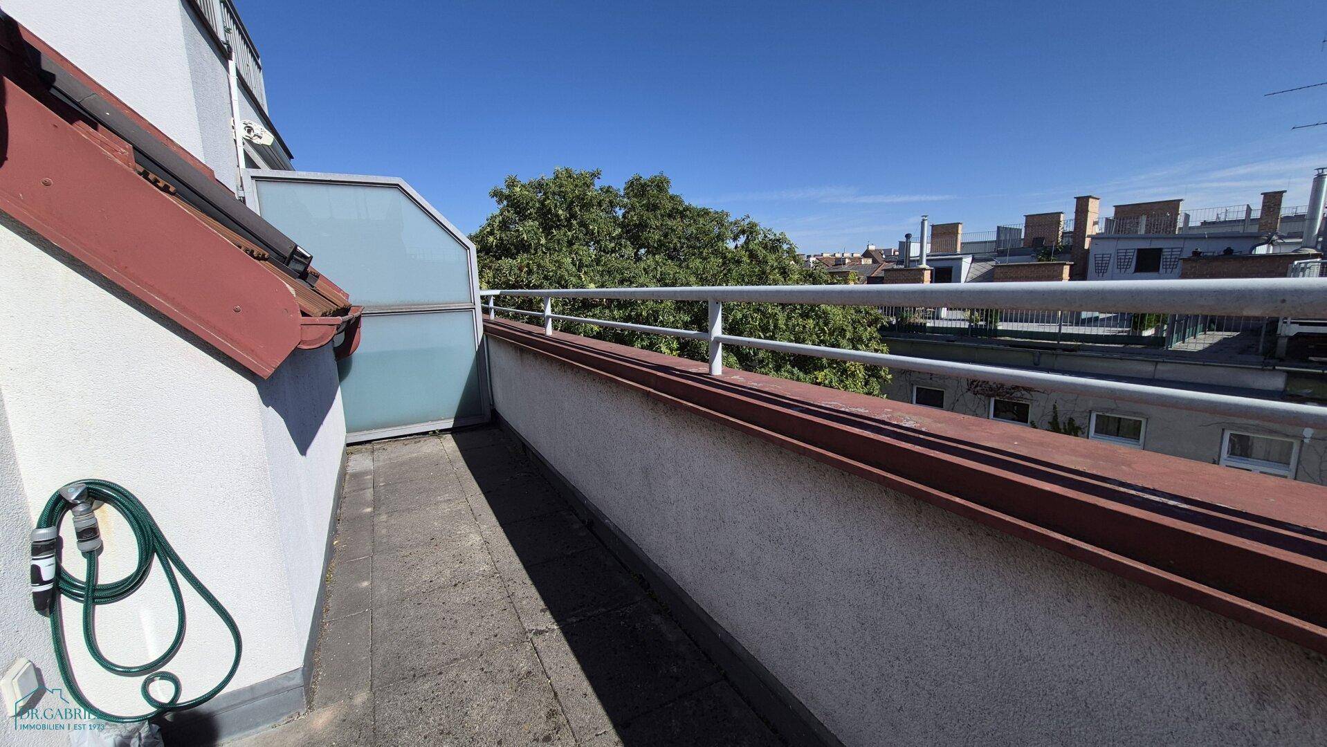 Sonniger Terrassenbereich mit Blick ins Grüne und einer praktischen Gartenschlauchhalterung.