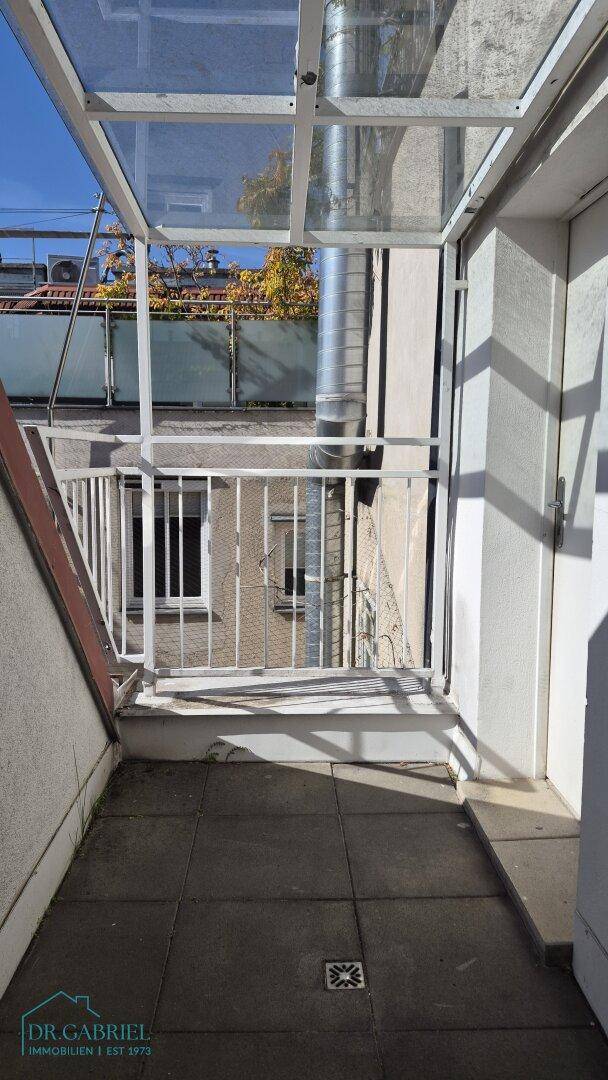 Kleiner überdachter Balkon mit Fliesenboden und Blick auf die umliegenden Gebäude.