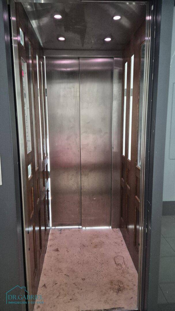 Innenansicht eines Aufzugs mit Metalltüren und Holzverkleidung.