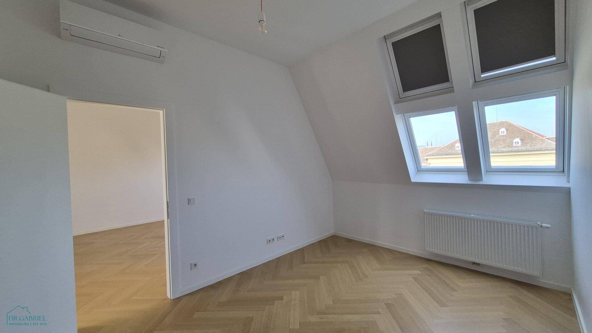 Unmöblierter Raum mit Fischgrätparkett, Dachfenstern und einem Heizkörper, bereit zur individuellen Gestaltung.